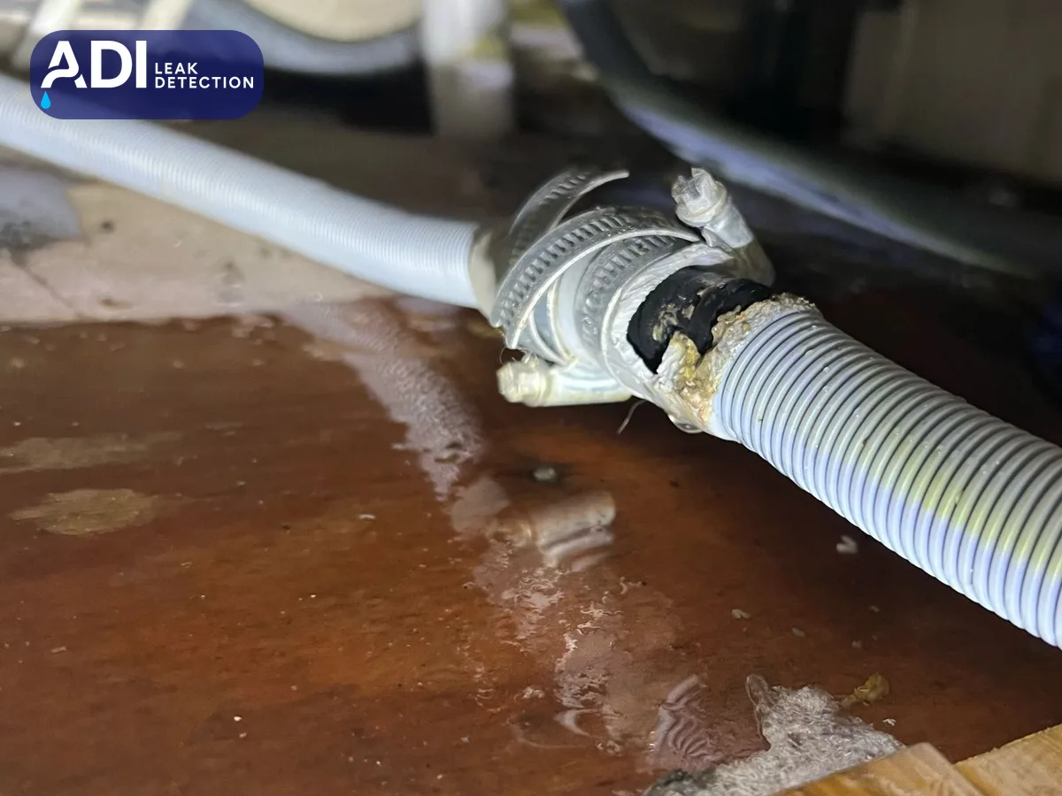 A washing machine waste hose with a torn, taped connection and water on the floor beneath it